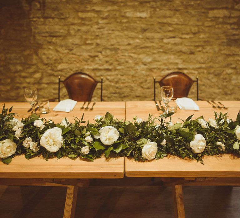 Sweetheart top table for wedding reception with white flowers and green foliage runner with gold cutlery