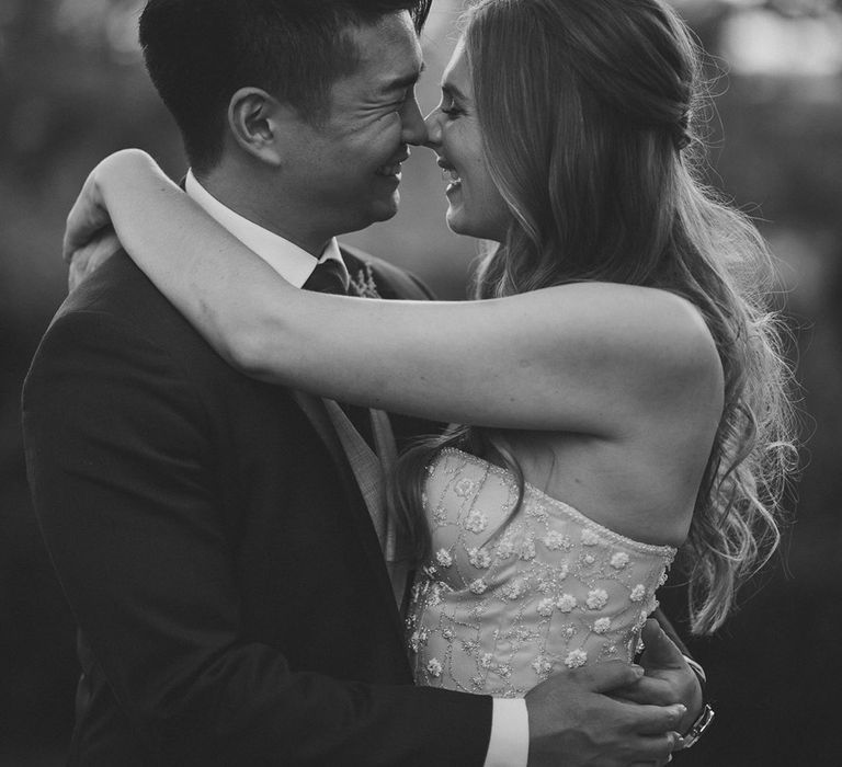 Bride and groom hug and smile together with bride in sparkly Pronovias strapless wedding dress and groom in blue suit and red tie