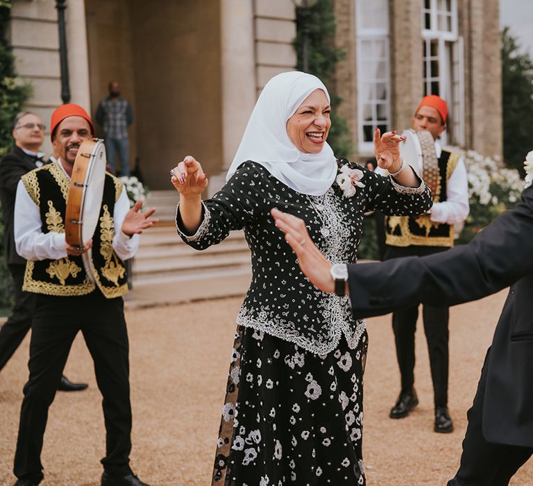 Groom in black tie dances with his mother with the Zaffa band 