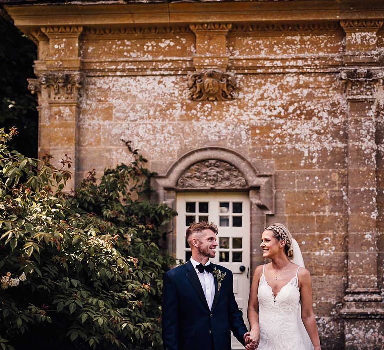 Bride and groom gaze at each other as they walk around their country house venue, Athelhampton House, together 