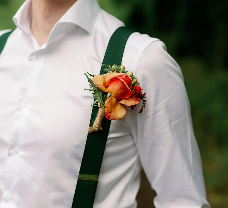 Groom wears open white shirt with green braces and brightly coloured floral buttonhole 