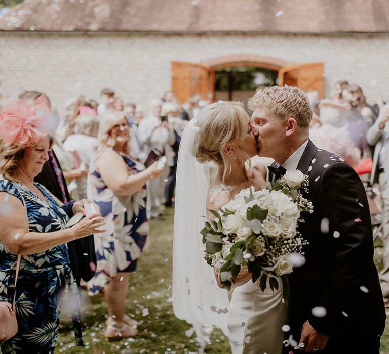 Bride and groom share a kiss at the end of their confetti exit from their ceremony 