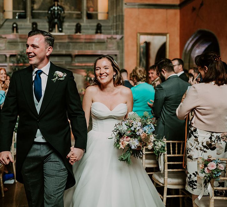 Bride & groom leave wedding ceremony surrounded by friends and family as bride holds pastel floral bouquet