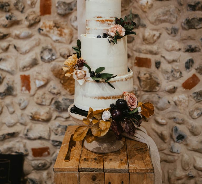 Four-tie rustic wedding cake with white frosting with autumnal flowers and a personalised cake topper 