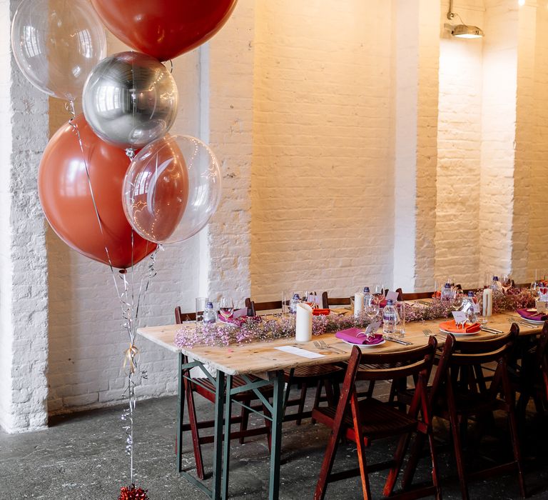 Orange, silver and see through balloons beside wooden banquet tables for orange and pink theme wedding 