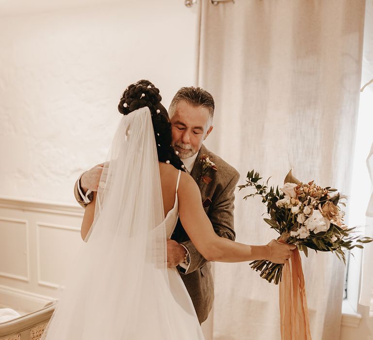 Bride hugs her father whilst holding dried floral bouquet tied with orange sheer ribbon