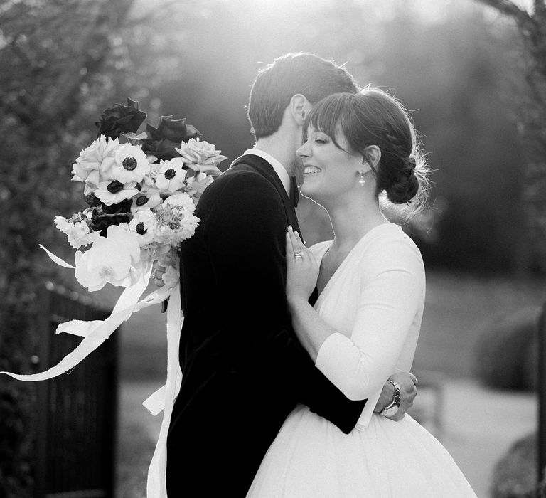 Bride wears her brown hair in low-bun and pearl drop earrings and princess tulle skirt wedding dress whilst kissing her groom outdoors 