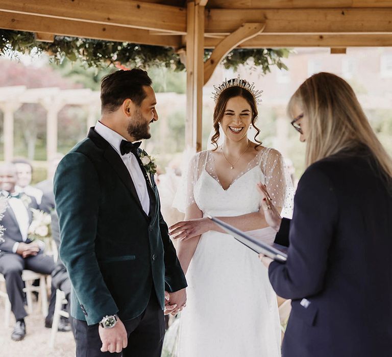 Bride and groom stand laughing under the gazebo for their outdoor ceremony 