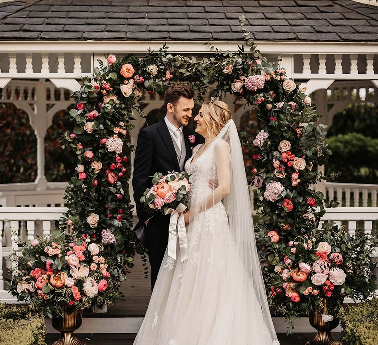 Bride and groom share an embrace in front of their pink flower arch altar decoration 