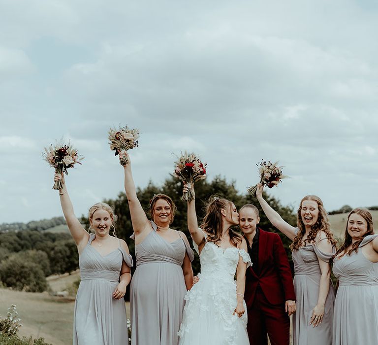 Bridesmaids in light grey off the shoulder with the bride in an off the shoulder wedding dress and bride in burgundy suit