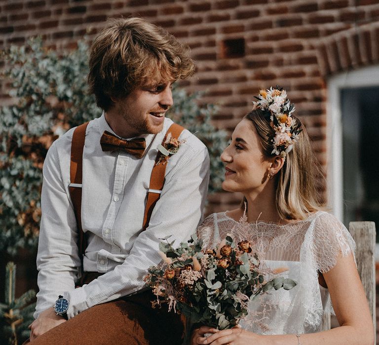 The bride and groom sit smiling at each other on their rustic boho wedding day 