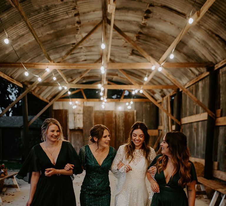 Bridesmaids in mismatched green bridesmaid dresses walking with the bride in a boho lace wedding dress 