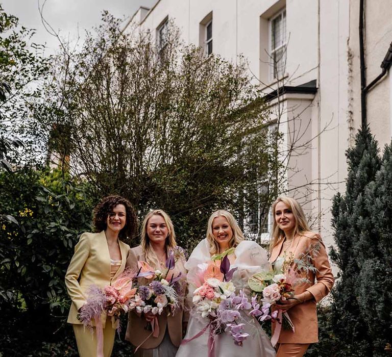 The bridesmaids wear different coloured suits standing next to the bride in a puff sleeve wedding dress 