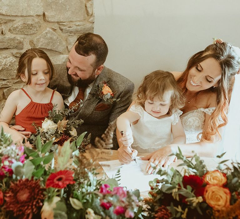 Bride and groom sign the wedding register with their daughters for autumn wedding 