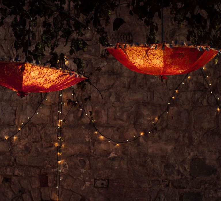 Colourful Indian umbrellas hang above tables finished with orange fabric table runners and colourful floral arrangements 