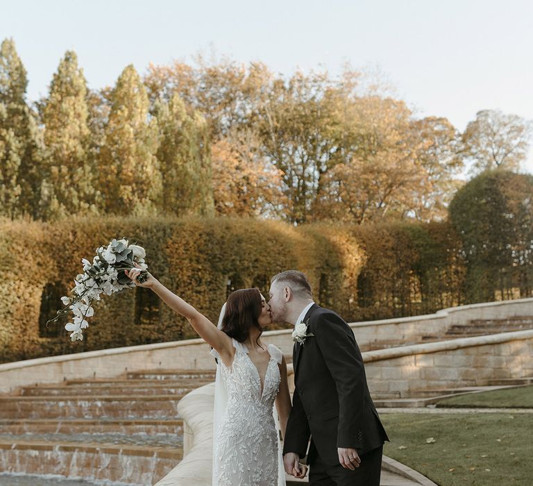 Bride in a fitted wedding dress holding a white orchid and rose bouquet kissing the groom in classic black suit for Newcastle wedding 