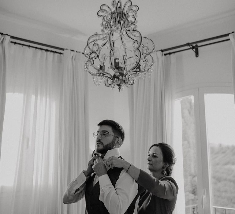 mother of the groom helping her son with his collar on the morning of the wedding 