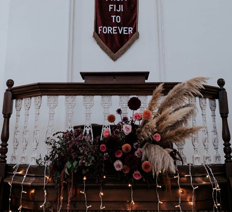 Brown fabric wedding banner, fairy lights and wildflower arrangement hanging above the altar at The Kings Chapel, Old Amersham