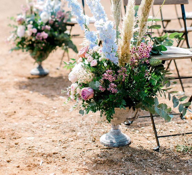 Pink wax flower, pink roses, baby blue delphinium and pampas grass in small white vases decorating the aisles for destination wedding in Italy