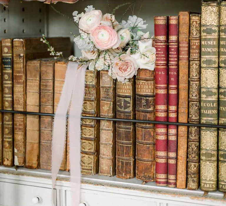 Spring inspired bridal bouquet with pink garden roses, peonies, baby's-breath and dried flowers sitting on a bookshelf with old, vintage books 