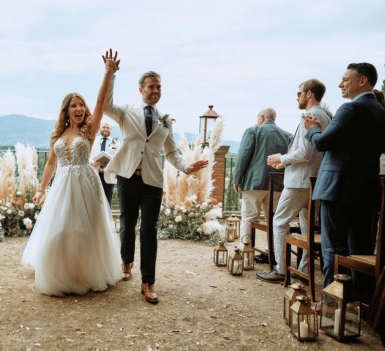 Bride in embroidered tulle wedding dress walking out of ceremony with groom in linen suit and cheering