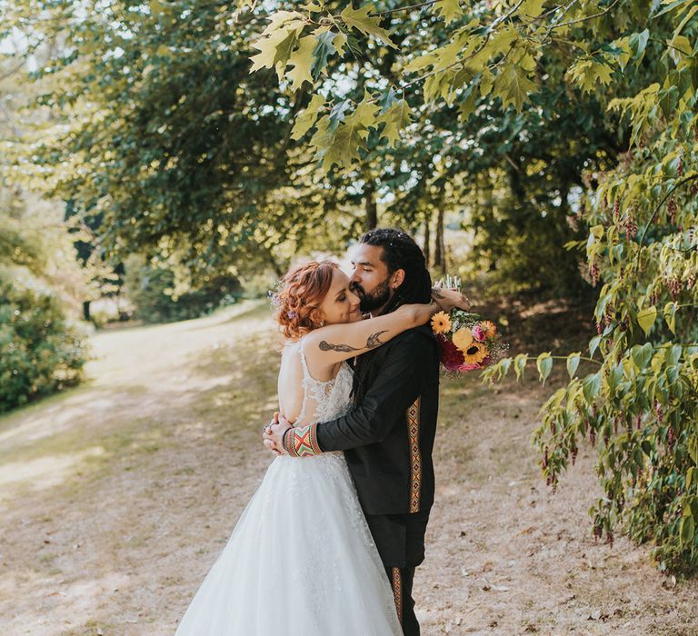 Bride in a lace wedding dress embracing her groom in a black outfit embracing 