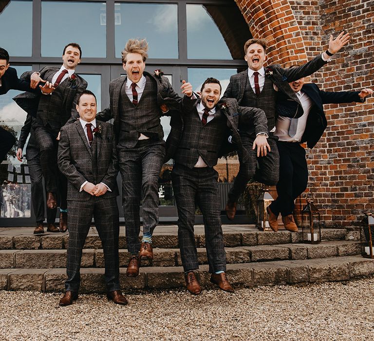 Groom and groomsmen in matching three piece grey checkered suits with red ties and red rose buttonholes 