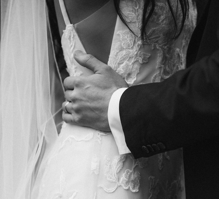 Groom holding bride by the waist in her a-line tulle wedding dress with beaded lace applique with petals 