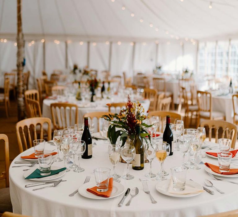 Classic wedding tablescape with dried orange and yellow flower and foliage wedding centrepieces on wooden tree trump circles in wedding marquee with fairy lights and festoon lighting