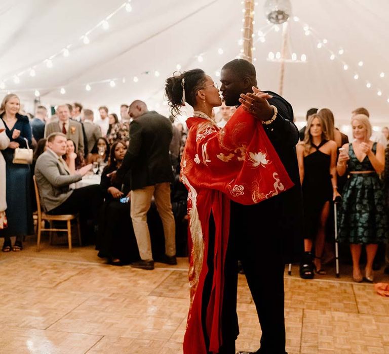 Bride in traditional red and gold Chinese silk kimono doing wedding first dance with groom in navy Nigerian traditional wedding outfit at Broadfield Court