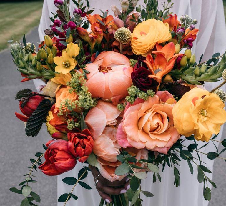 Colourful bridal bouquet with pink, orange and yellow garden roses, peonies, poppies, burflowers, and eucalyptus 