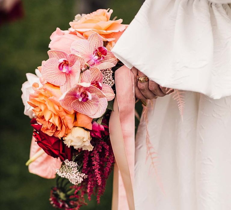 Bride holding the pink wedding bouquet with orchids and anthuriums tied with pink ribbon 