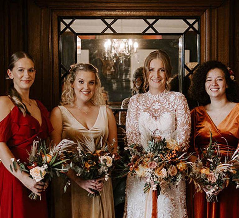 Bride in boho long sleeve lace wedding dress with bridesmaids in autumnal dresses in warm tones