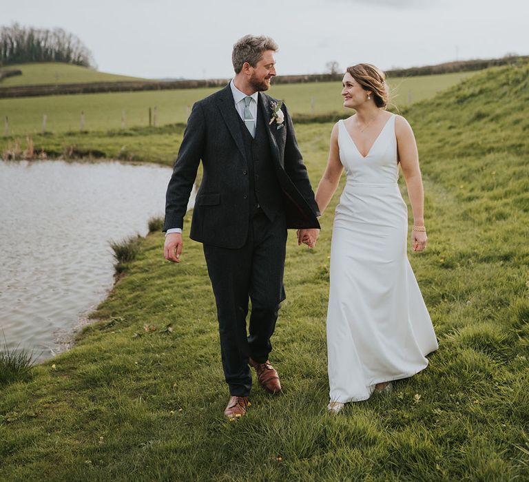 Groom in three piece dark wedding suit with light green tie walking hand in hand with the bride in plunging wedding dress 