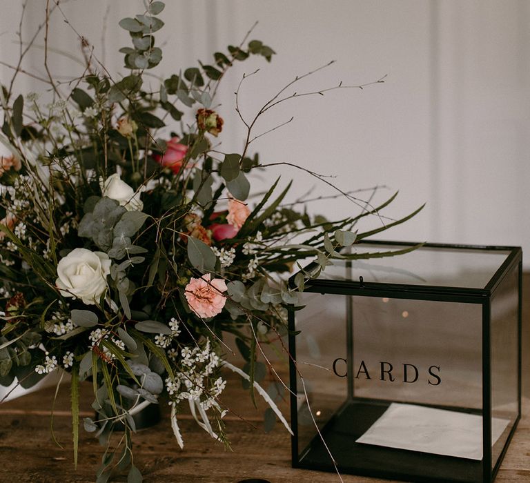 Transparent black and glass card box for the guests next to a pretty pink and white wedding flower arrangement 