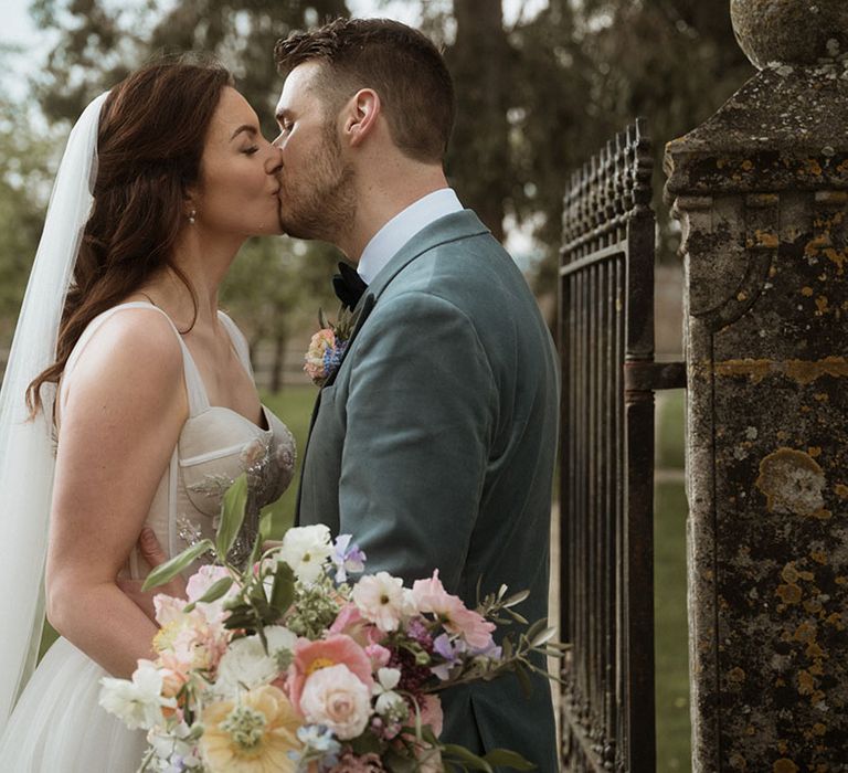 The groom in a powder blue velvet blazer kisses the bride for their cute couple wedding portraits 