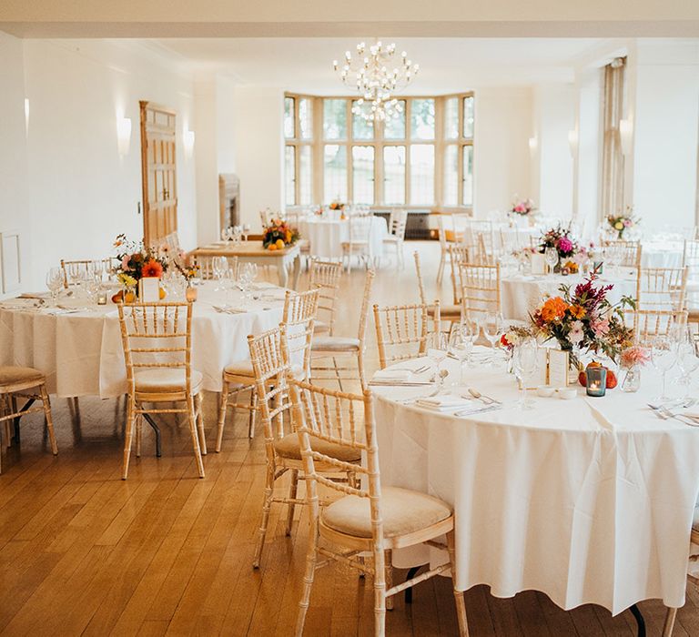 White wedding table cloths and napkins with autumnal seasonal table centrepieces with gold framed table number signs 