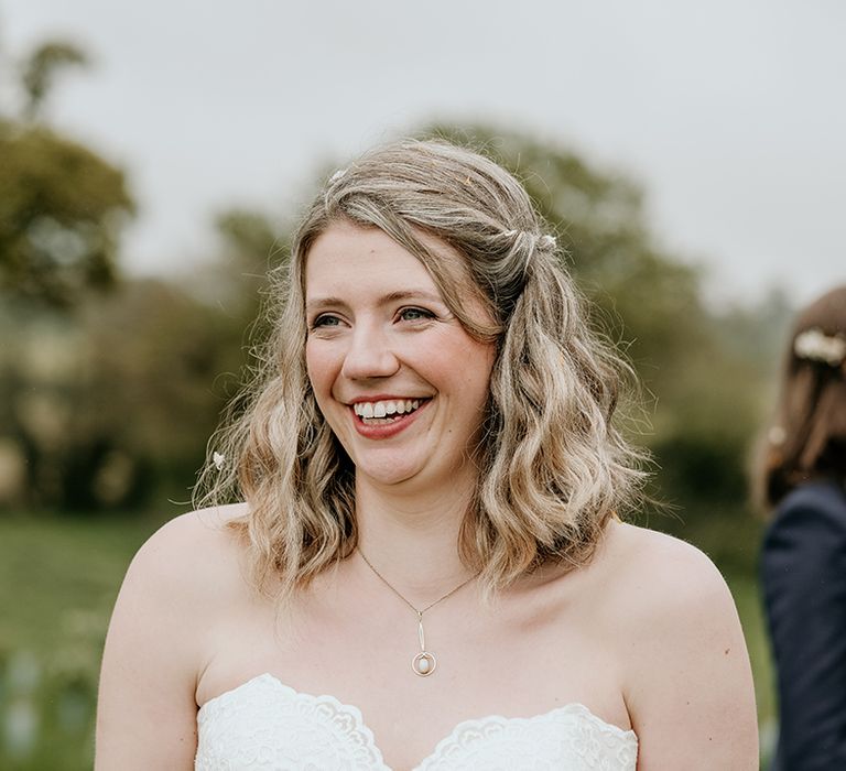 blonde bride with wavy bobbed hair smiling wearing a strapless lace wedding dress