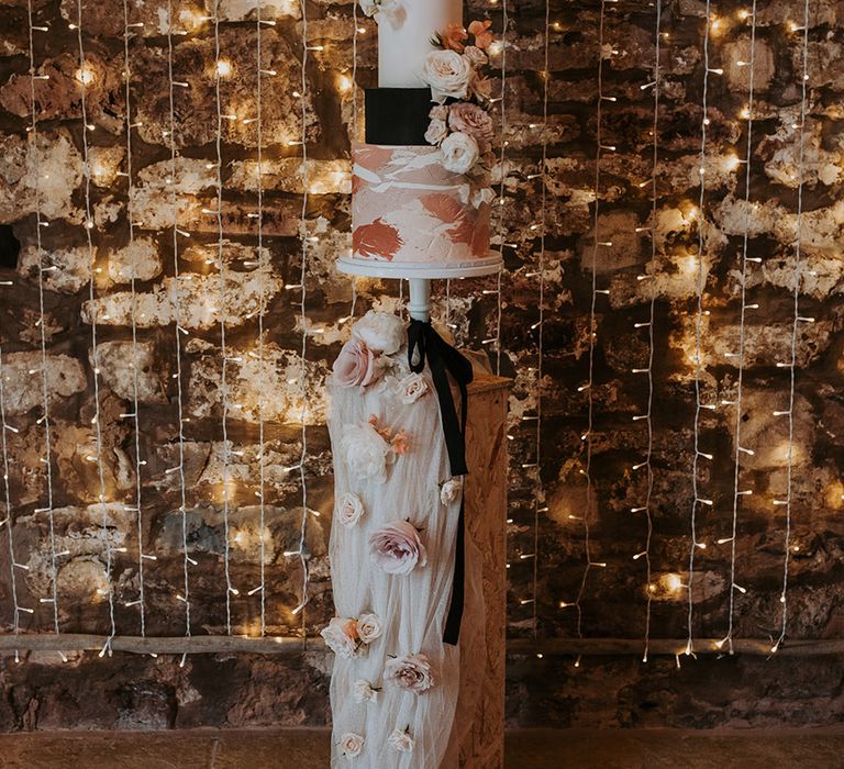 Pink, black, and white four tier wedding cake on stand with pink wedding flower decorations 