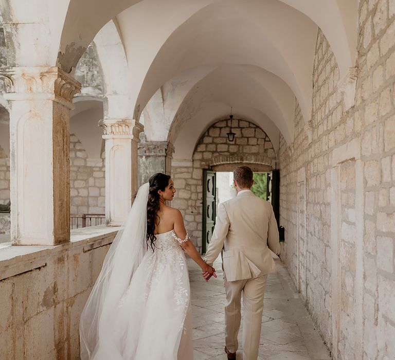 bride in 3D lace wedding dress and groom in linen suit walk through monastery in Croatia after wedding ceremony