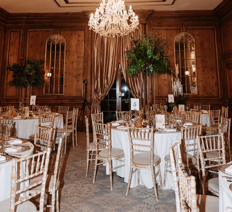 Luxe chandelier hanging above the round wedding tables with tall tale centrepiece flowers 