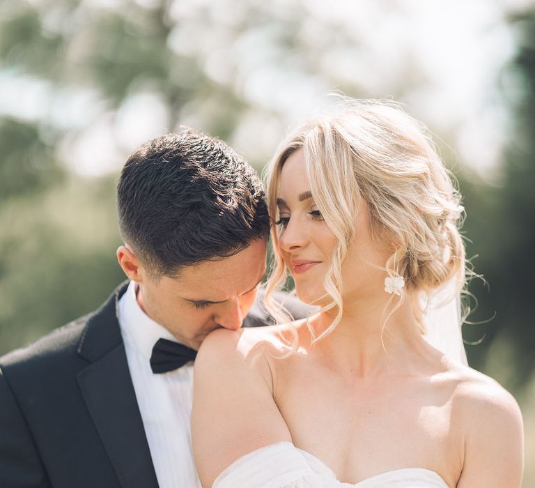 Groom in tuxedo kissing his brides shoulder in strapless wedding dress