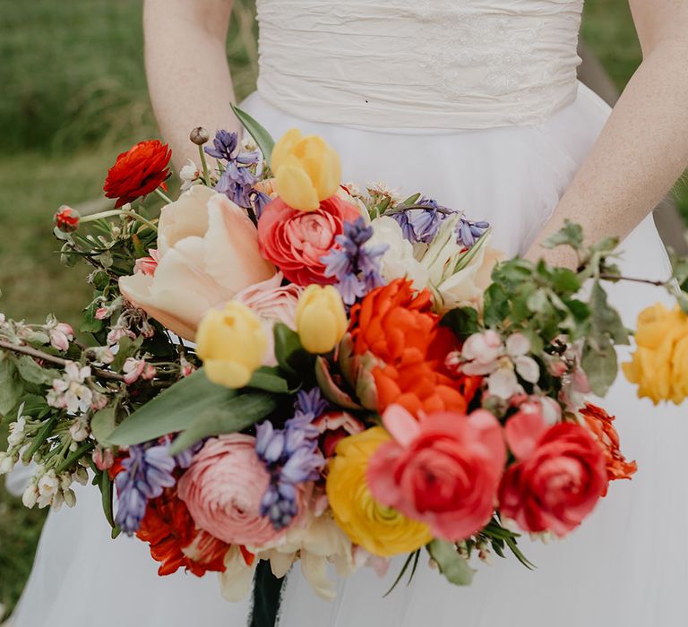 Bride wearing fitted wedding dress holding orange, yellow and pink wedding bouquet 