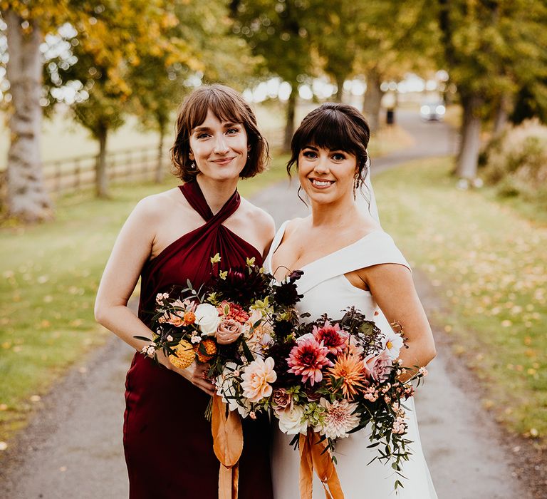 Bridesmaid in burgundy halterneck bridesmaid dress standing with the bride in off the shoulder custom wedding dress