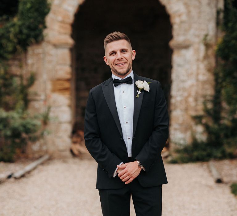 Groom in black tuxedo with white flower buttonhole traditional groom fashion 