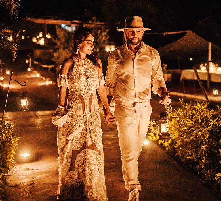 Bride and groom walk together around the softly lit wedding venue 