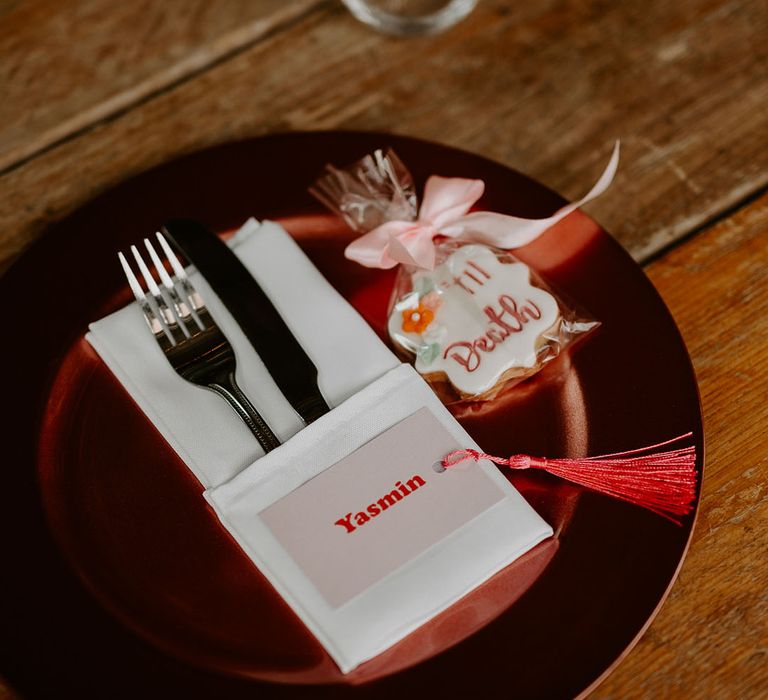 Pink retro disco theme wedding with pink wedding place setting including a pink place name card, pink iced biscuit favour and red charger plate