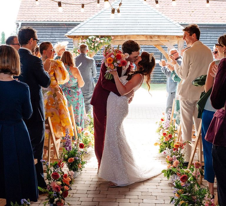 Bride and groom share a kiss as they walk back down the aisle as a married couple at outdoor ceremony 