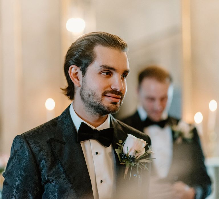 Groom wearing black bow tie and silk pattered suit with blush pink button hole flower 