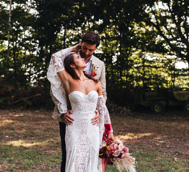 Bride & groom embrace in fields with floral bouquet